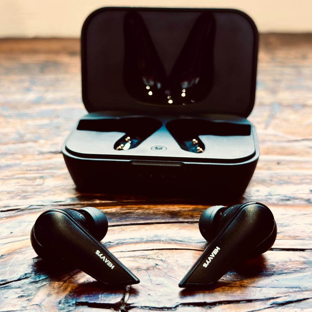 Black wireless earbuds with charging case on a wooden surface